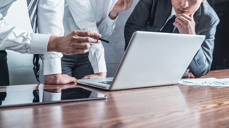 three men analyzing something on the laptop screen